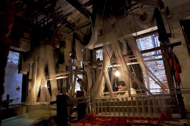 A weaver working at a wooden handloom threaded with coloured yarn